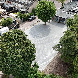 Een nieuw betegeld plein tussen woningen en een schoolgebouw, met bomen die midden in de bestrating zijn uitgespaard.